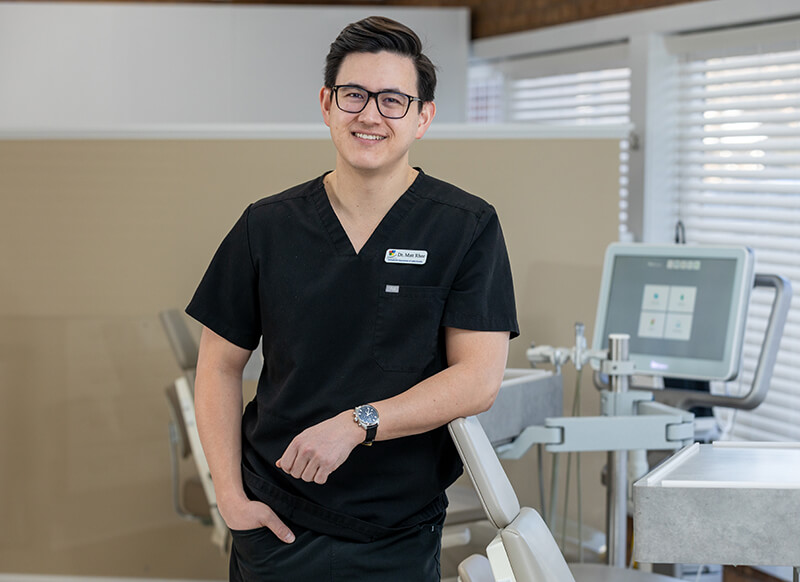 Dr. Matthew Rhee, smiling in black scrubs and glasses in a dental office