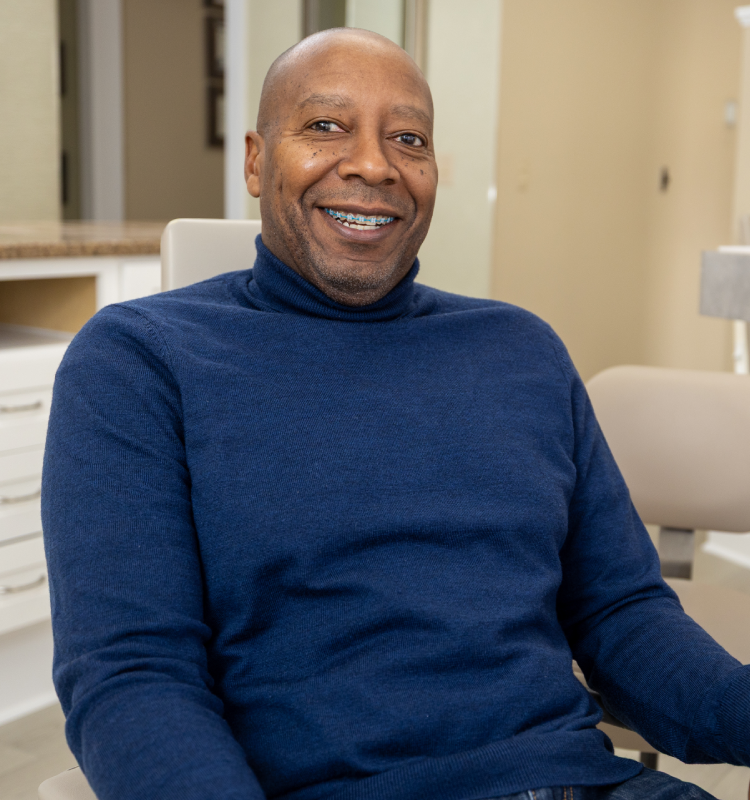 Smiling man with braces in a blue turtleneck seated in a dental chair