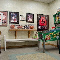 Waiting room with framed basketball jerseys, signed basketballs on a shelf, and a pinball machine